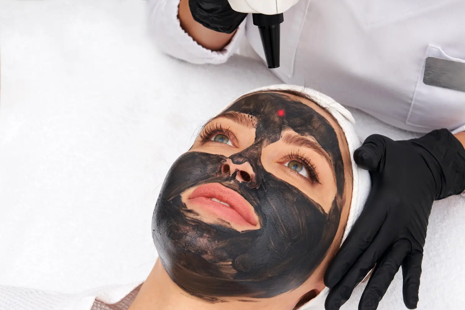 Kosmetikerin trägt einer schönen Frau eine schwarze Maske für ein Carbon-Peeling auf