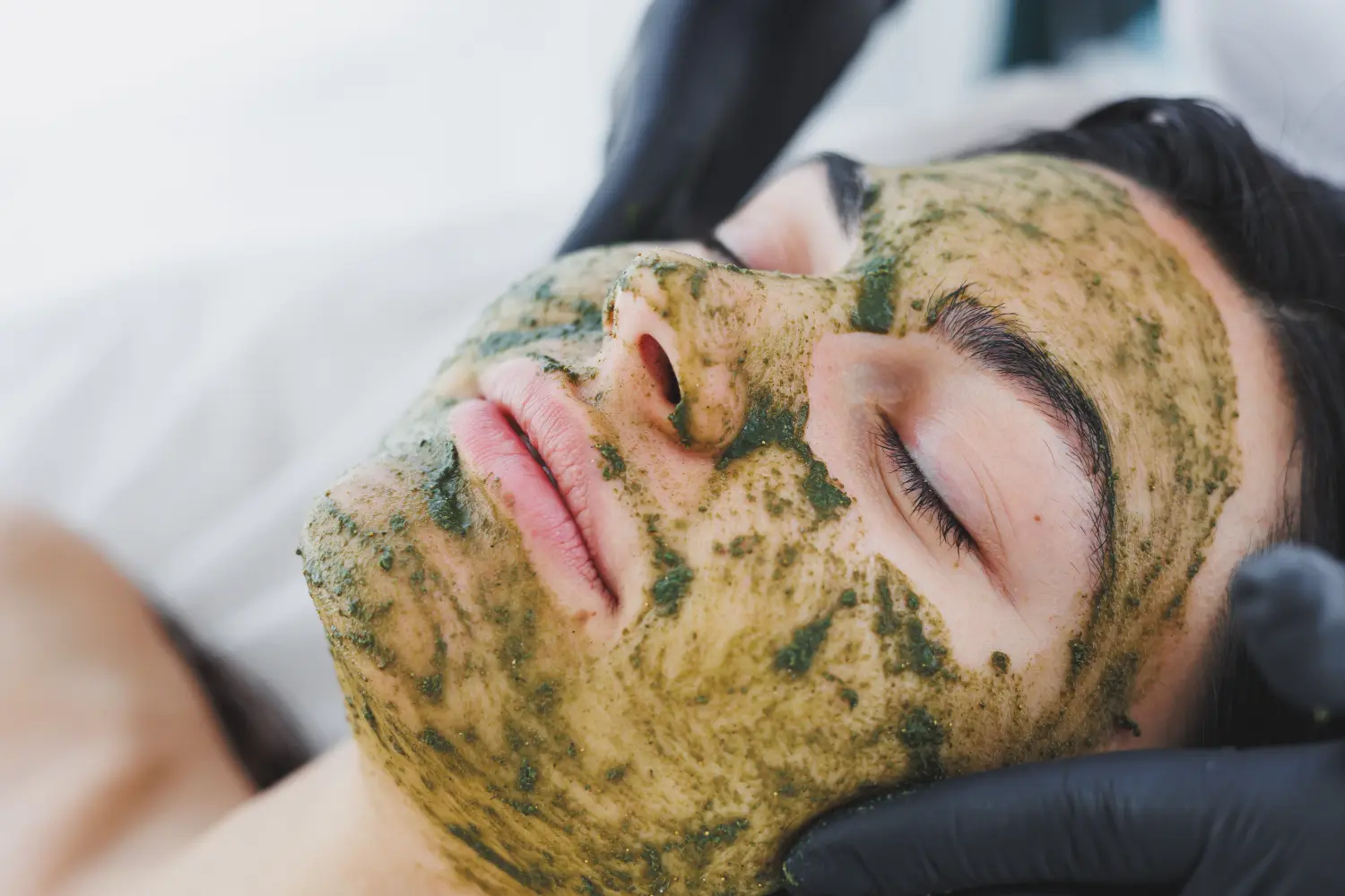 Eine Kosmetikerin macht eine Maske auf dem Gesicht einer Frau. Maskenpeeling für das Gesicht, Spa-Behandlungen, Hautpflege. Eine Frau erhält Gesichtspflege von einer Kosmetikerin